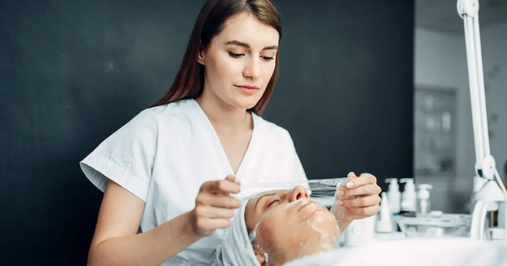 Esteticista: guia completo sobre a profissão - Esteticista faz máscara facial para jovem mulher