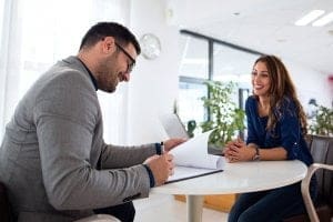 pretensão salarial processo seletivo - homem entrevistando jovem mulher e olhando seu currículo