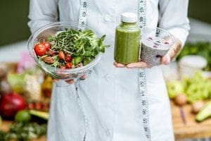 Mulher segurando legumes em frente a uma bela mesa repleta de alimentos - Técnico em Nutrição e Nutricionista