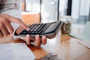 homem utilizando a calculadora com papéis e moedas na mesa - Cursos para melhorar seu currículo