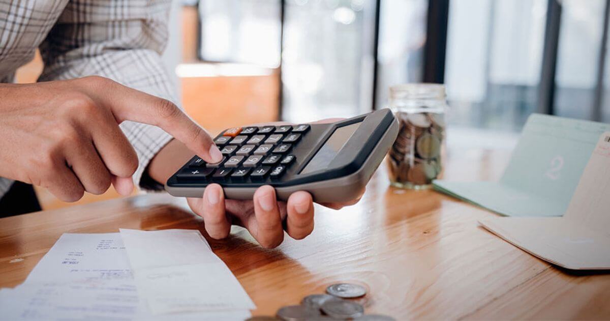 homem utilizando a calculadora com papéis e moedas na mesa - Cursos para melhorar seu currículo