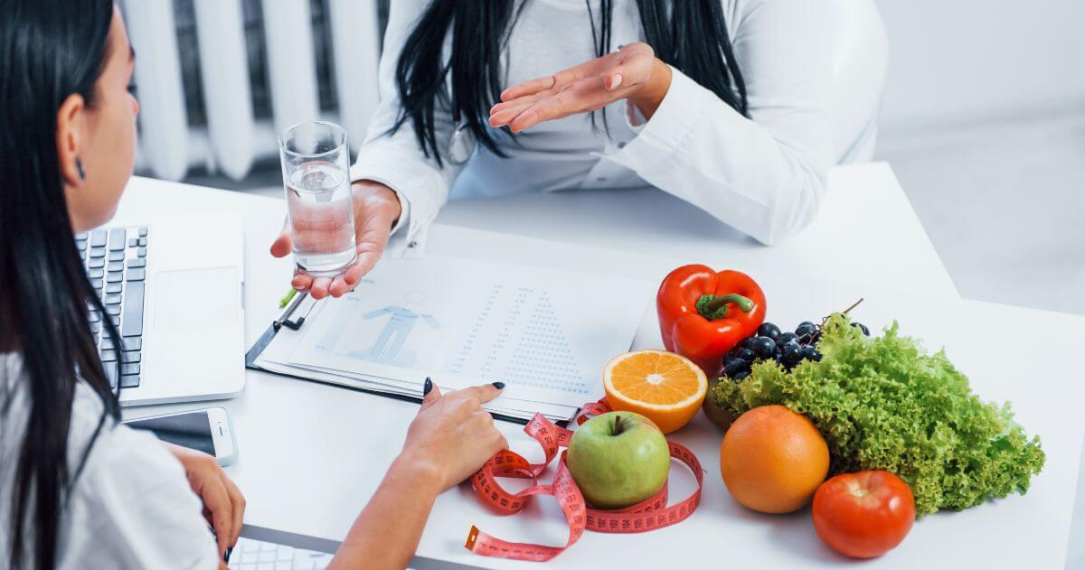 Nutricionista atendendo paciente com mesa repleta de frutas e verduras - Mensalidade de Nutrição