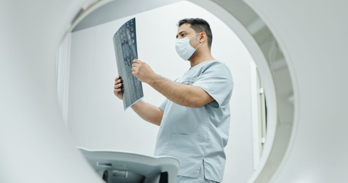 Técnico em Radiologia de etnia mista madura séria em máscara e uniforme olhando imagem de raio-x - Como funciona o Curso Técnico em Radiologia
