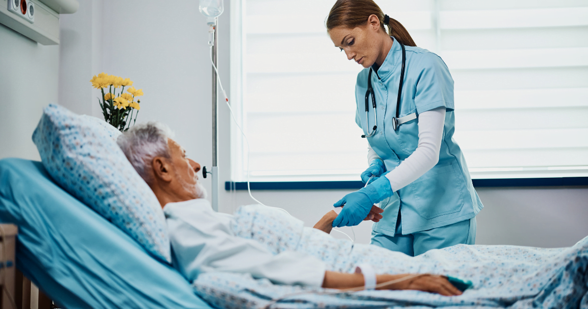 Enfermeira de meio adulto verificando gotejamento intravenoso de paciente sênior na enfermaria do hospital - A importância das Aulas Práticas no Curso Técnico em Enfermagem