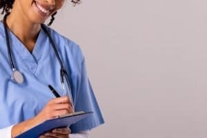 Técnico ou Auxiliar de Enfermagem: qual a melhor opção? - Técnica em Enfermagem com estetoscópio escrevendo na área de transferência